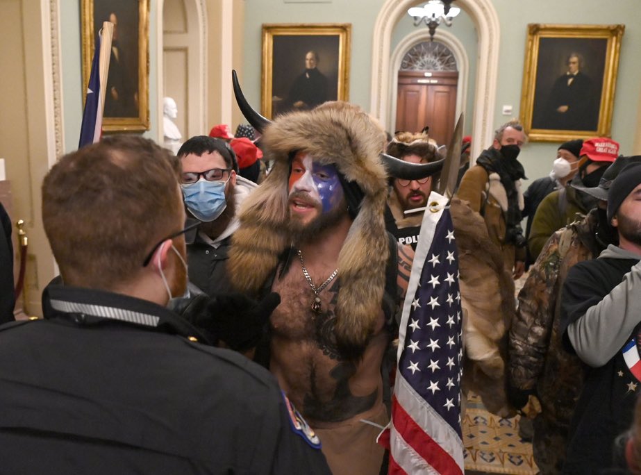 A mob of people dressed in animal skins and "Make America Great Again" hats confront Capitol police officers while storming the Legislative building of the Government.